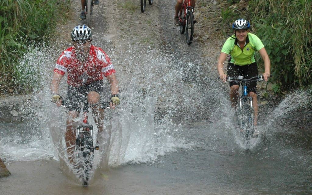 A man and a woman mountain biking through a river in Costa Rica